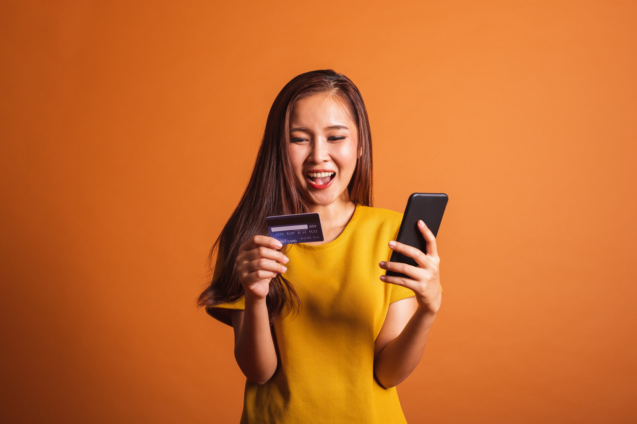 Young Asian woman using credit card and smart phone for online shopping, payment over orange background